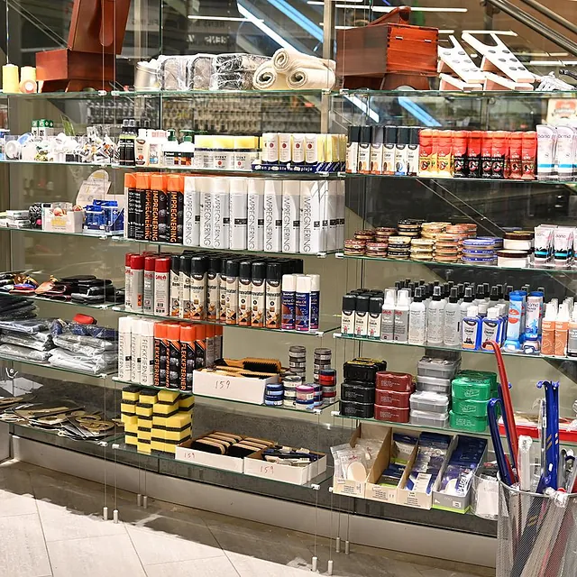 Glasshylle fylt med skopleieprodukter, belter, skosåler og impregneringsspray i butikken.