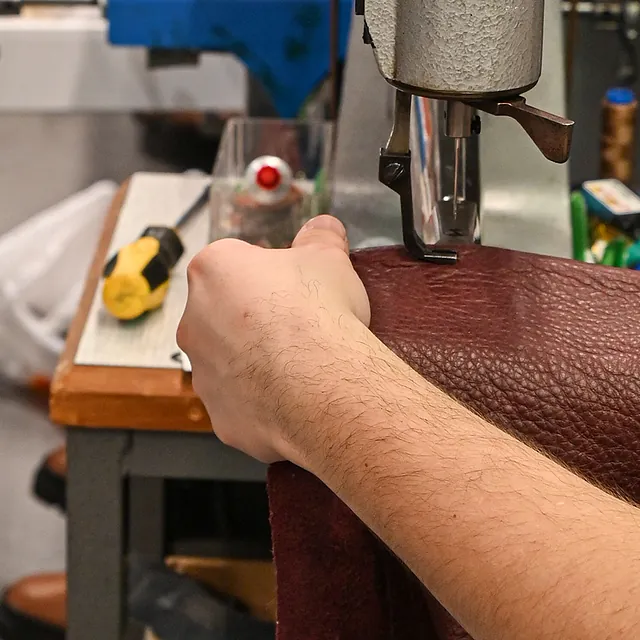 Hånd syr et stykke mørkerødt skinn med en industriell symaskin.